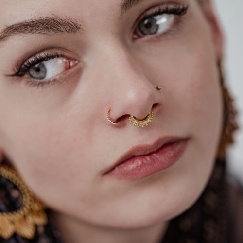 Nahaufnahme eines Gesichts mit goldenem Septum Clicker und Ohrring