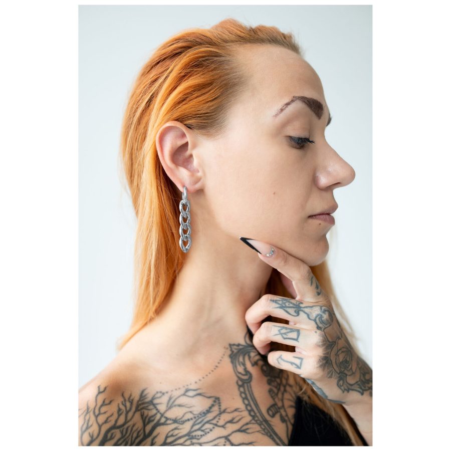 Silberne Ohrringe im Kettendesign getragen an einem Ohr mit tätowierter Hand und rotem Haar
