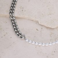Silberne Gliederkette kombiniert mit synthetischen Perlen auf hellem Steinuntergrund