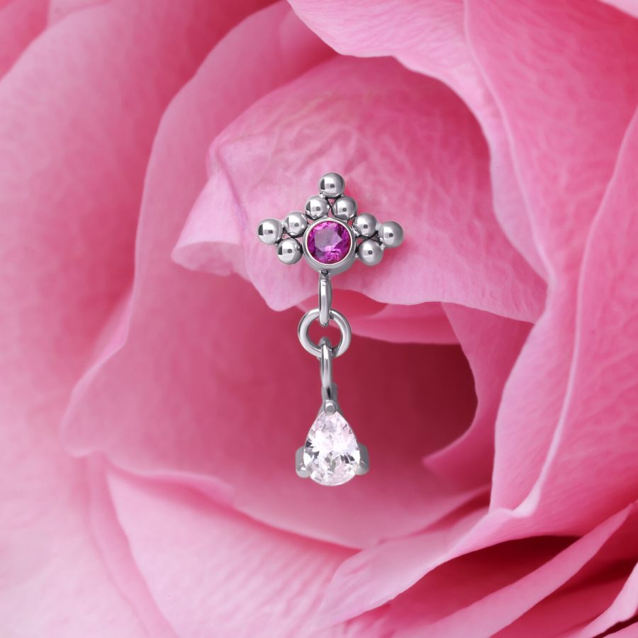 Silberner Piercing Anhänger mit rotem Kristall und Tropfenform Anhänger vor rosa Blütenblatt