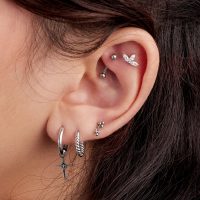 Nahaufnahme eines Ohres mit mehreren Piercings, darunter ein hängender Titan-Aufsatz und andere silberne Schmuckstücke.