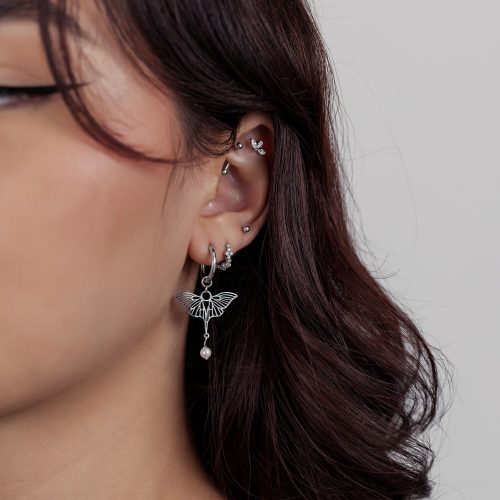 Frau mit mehreren silbernen Ohrpiercings und einem Schmetterlingsanhänger auf hellem Hintergrund