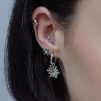 Nahaufnahme eines Ohrs mit mehreren silbernen Piercings in verschiedenen Designs und Kristallen