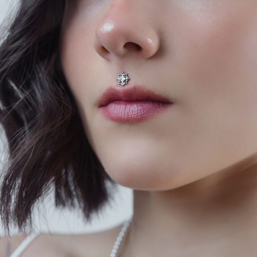 Nahaufnahme eines silbernen Kristall-Piercing-Aufsatzes am Medusa-Piercing einer Frau auf neutralem Hintergrund