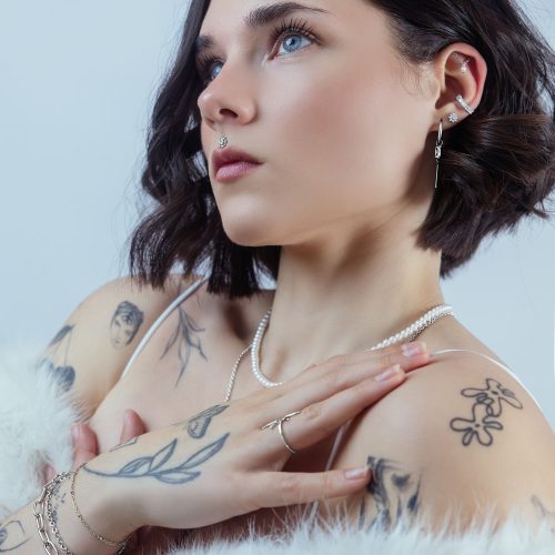 Frau mit Ice Flower Kristallaufsatz im Ohr, silberne Farbe, vor neutralem Hintergrund