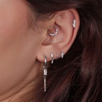Nahaufnahme eines Ohres mit mehreren silbernen Piercings, einige mit Kristallen besetzt
