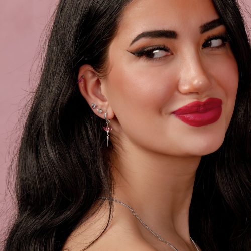 Frau mit langen schwarzen Haaren und silbernem Ohrring mit rotem Rubin auf rosafarbenem Hintergrund
