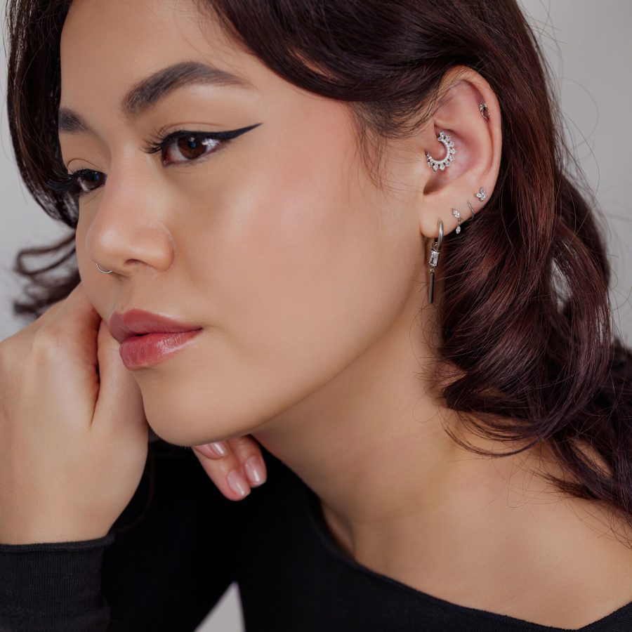 Frau mit mehreren silbernen Piercings, darunter ein mondförmiges Design am Ohr auf hellem Hintergrund