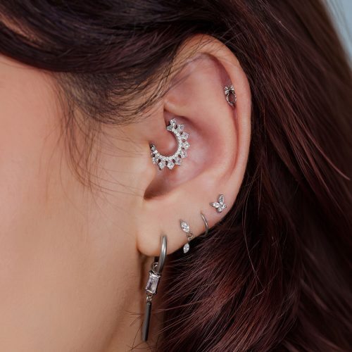 Nahaufnahme eines Ohres mit mehreren silbernen Piercingaufsätzen und Schmuckstücken.