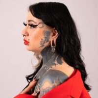 Frau mit Tattoos trägt schwarzes und silbernes Ohrgewicht, rote Kleidung