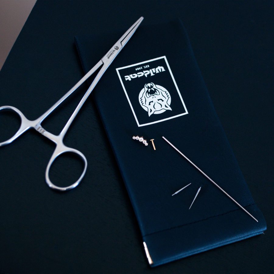 Piercing-Set mit Zange, Nadeln und Kleinteilen auf schwarzem Hintergrund