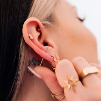 Nahaufnahme eines Ohrs mit mehreren goldenen Piercings und Schmuckstücken, Hand hält das Ohr