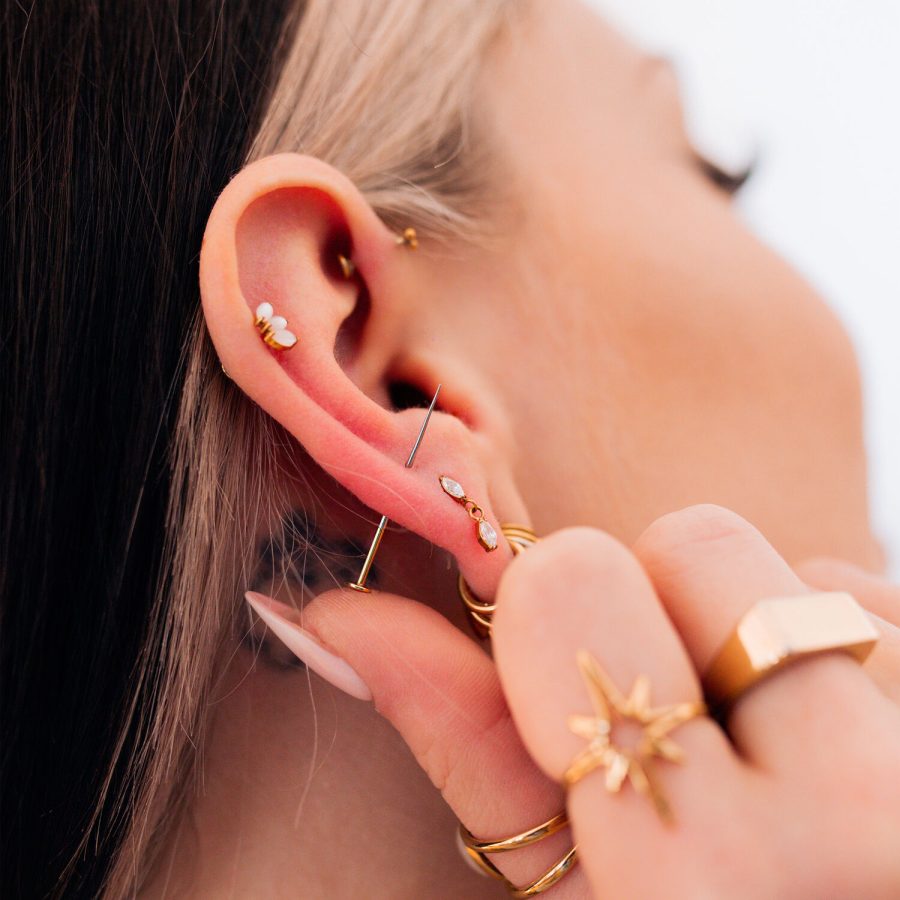 Nahaufnahme eines Ohrs mit mehreren goldenen Piercings und Schmuckstücken, Hand hält das Ohr