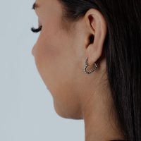 Frau mit seitlichem Blick trägt silberne Herz-Ohrringe vor grauem Hintergrund