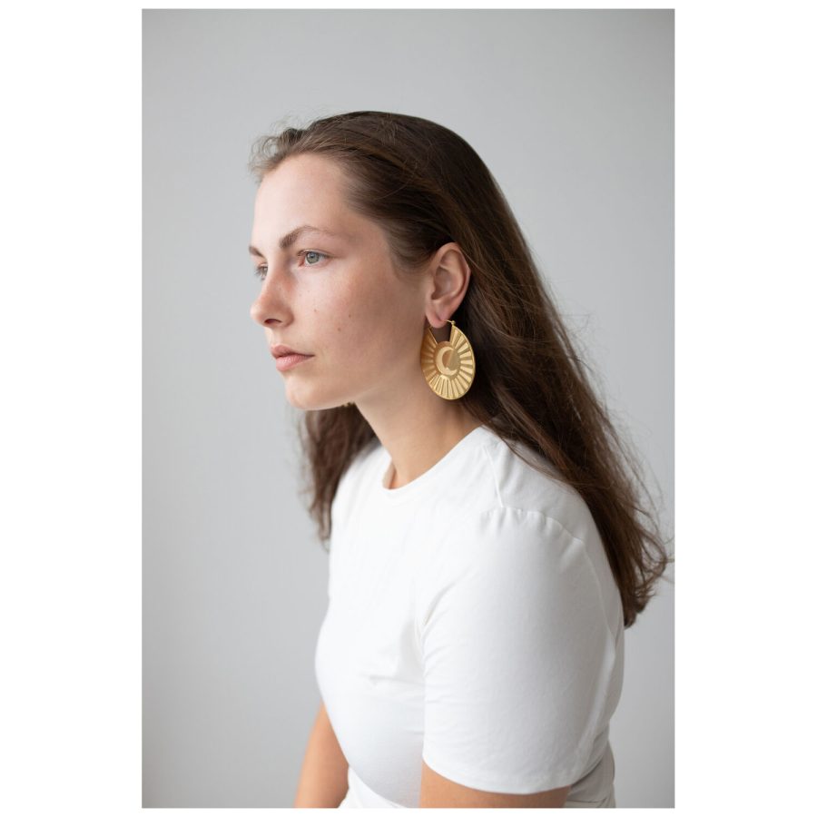 Frau mit goldenen Moonshine Hoops Ohrringen vor grauem Hintergrund