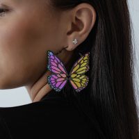 Frau mit bunten Schmetterling-Ohrringen aus schwarzem Chirurgenstahl auf hellem Hintergrund