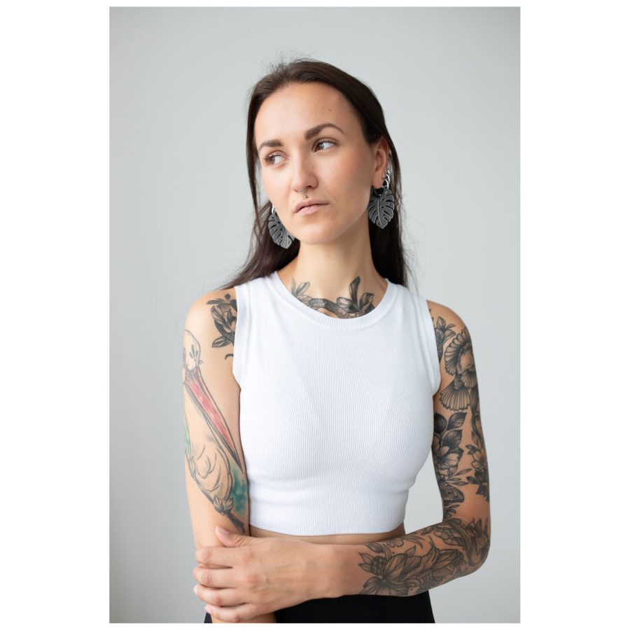 Frau mit tätowierten Armen trägt Monstera Leaf Hoops Ohrringe, weißes Top