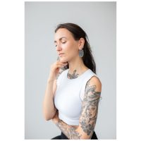 Frau mit tätowiertem Arm trägt silberne Floral Nautilus Hoops vor grauem Hintergrund