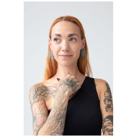 Frau mit roten Haaren trägt silberne Mandala Ohrringe, Tattoos sichtbar