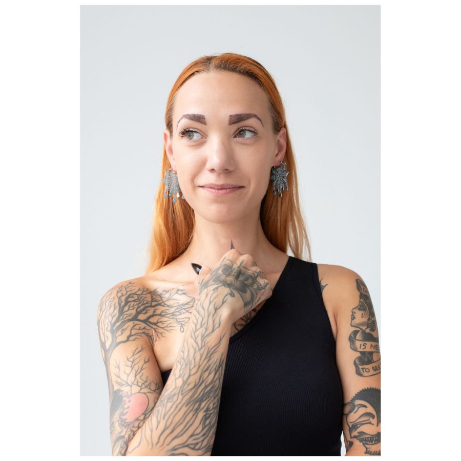Frau mit roten Haaren trägt silberne Mandala Ohrringe, Tattoos sichtbar