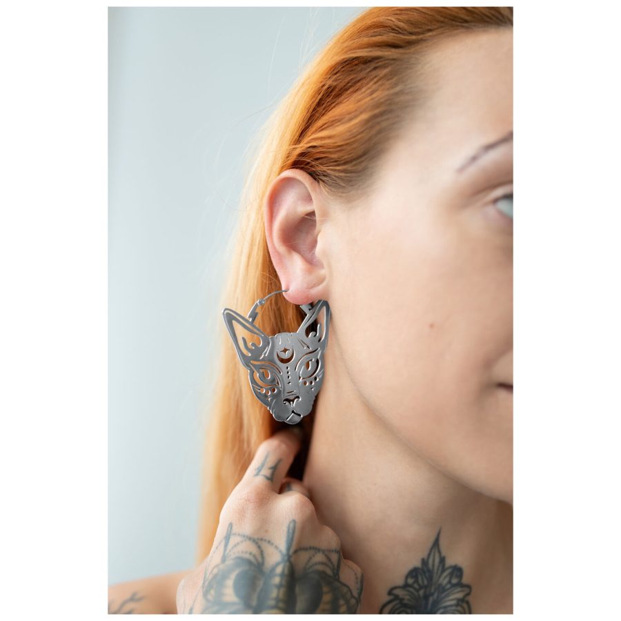 Silberne Sphynx Hoops Ohrringe an einem Ohr mit tätowierter Hand