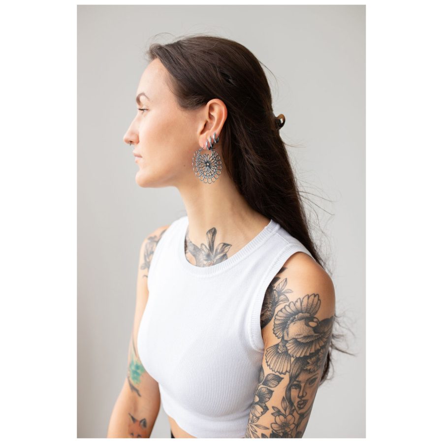 Frau mit Daisy Hoops Ohrringen in Schwarz und Silber vor grauem Hintergrund