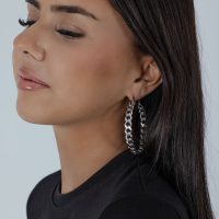 Silberne Curbchain Hoops Ohrringe an Frau mit dunklem Haar vor neutralem Hintergrund