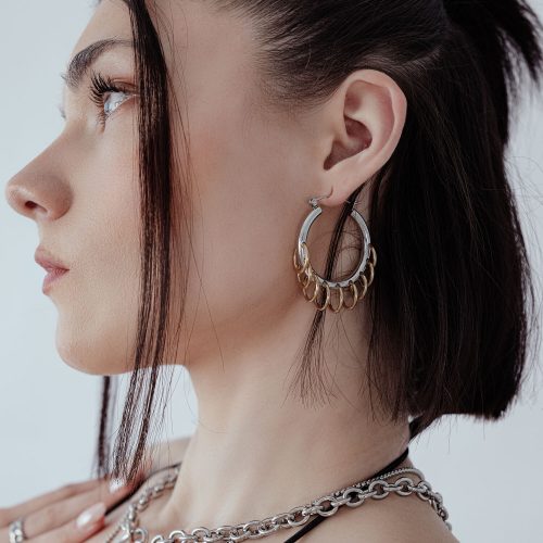 Frau mit stilvollen, massiven Hoops mit Loops in Silber und Gold vor weißem Hintergrund