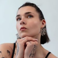 Frau mit kurzen Haaren trägt große, filigrane Ohrringe aus silbernem Metall vor hellem Hintergrund