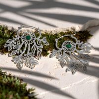 Zwei silberne Ohrringe mit filigranen Ornamenten und grünen Steinen auf einer weißen Oberfläche mit Moos
