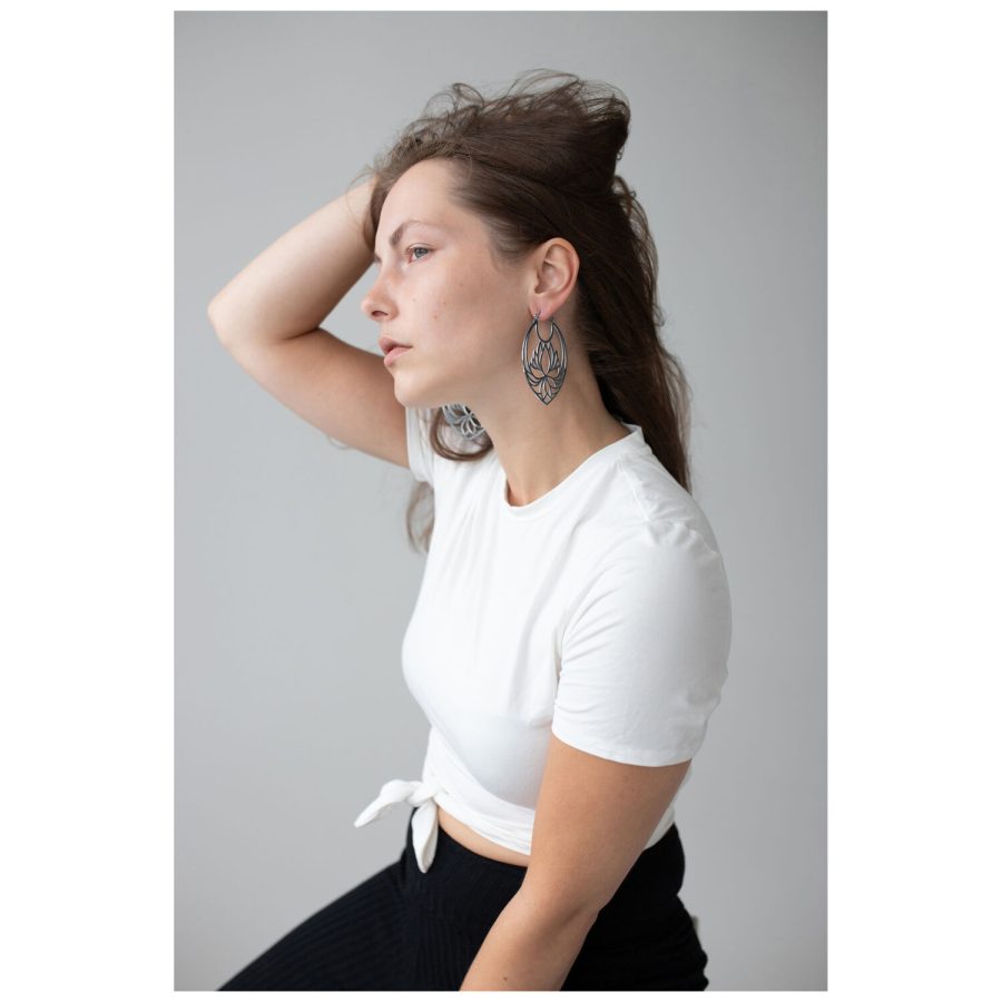 Frau mit Lotus Hoops Ohrringen aus Edelstahl in Schwarz und Silber auf grauem Hintergrund