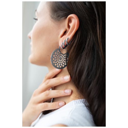 Frau trägt große, runde Ohrringe in Schwarz-Silber mit filigranem Design.