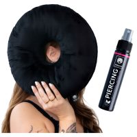 Schwarzes Piercingkissen mit Loch, gehalten von Person, daneben Piercingspray