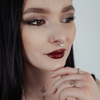 Frau mit schwarzem Haar trägt silbernen Septum Clicker mit Opal auf hellem Hintergrund
