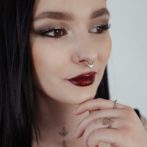 Frau mit schwarzem Haar trägt silbernen Septum Clicker mit Opal auf hellem Hintergrund