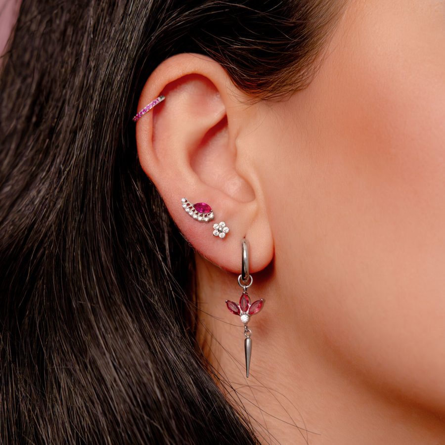 Silberner Ohrring am Ohr mit roten Kristallen und mehreren Piercings in einem Ohr
