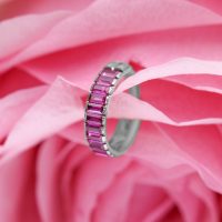 Silberner Piercing-Ring mit roten Baguette-Kristallen auf rosa Blütenhintergrund
