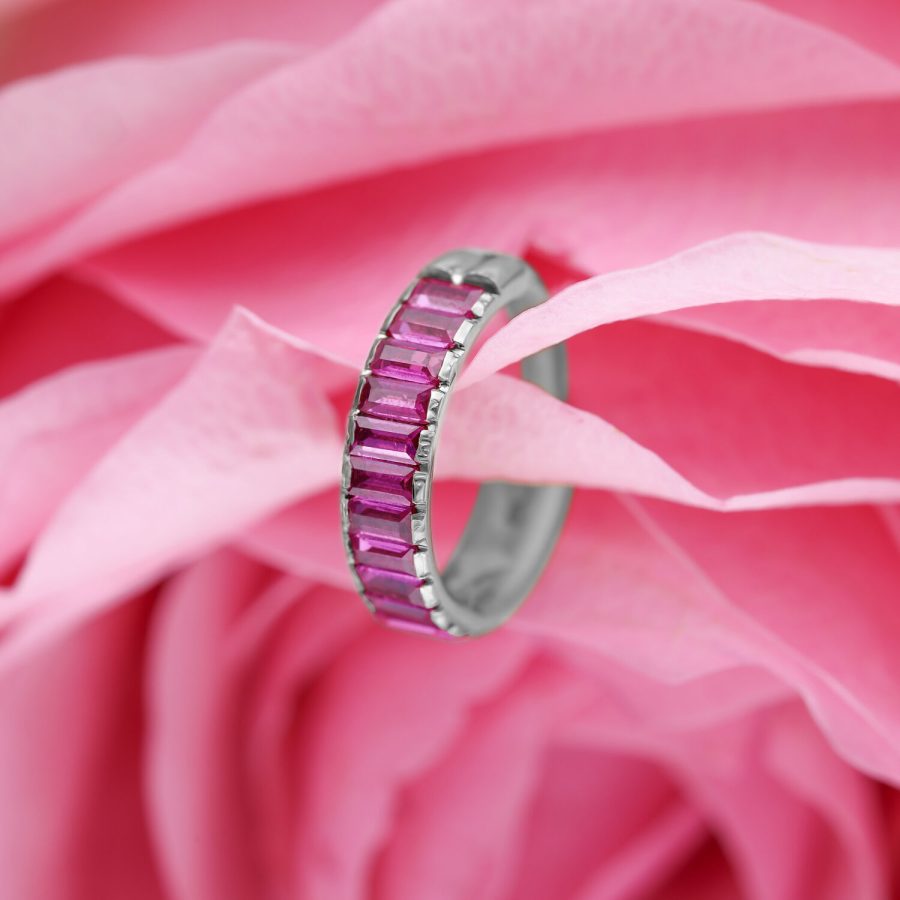 Silberner Piercing-Ring mit roten Baguette-Kristallen auf rosa Blütenhintergrund