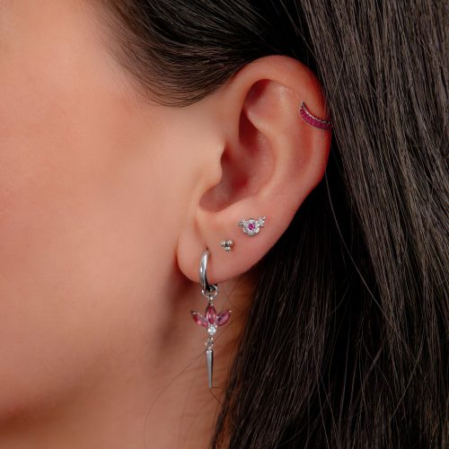 Ohr mit mehreren Piercings, darunter ein silberner Clicker mit roten Kristallen.