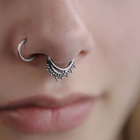 Nahaufnahme eines silbernen Triple Oriental Clickers im Septum eines Gesichts