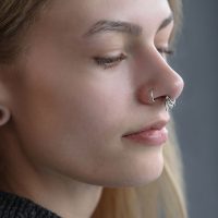 Nahaufnahme eines silbernen Triple Oriental Clickers im Septum einer Person