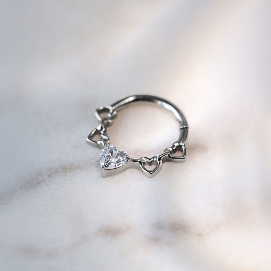 Silberner Septum Clicker aus Titan mit Herzdesign und Kristallen auf marmoriertem Hintergrund