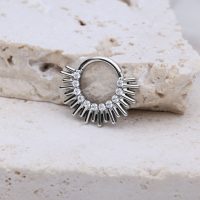 Silberner Septum Clicker mit Strahlen-Design auf hellem Steinuntergrund