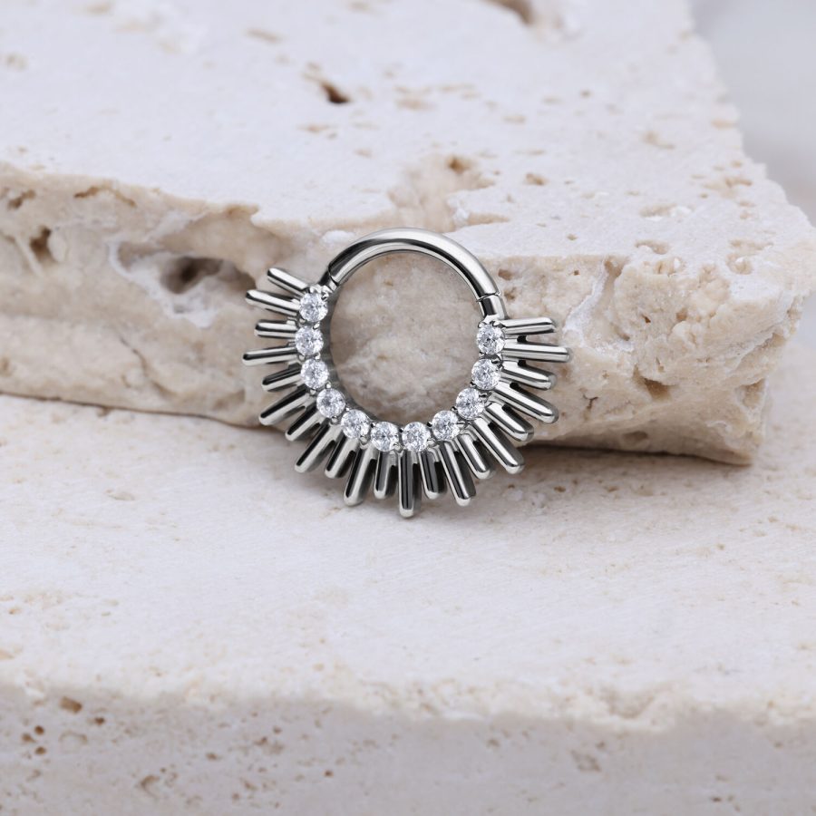Silberner Septum Clicker mit Strahlen-Design auf hellem Steinuntergrund