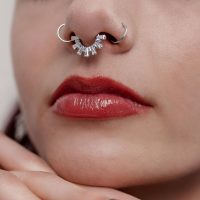 Nahaufnahme eines silbernen Septum Clickers mit Kristallen in einer Nase, rote Lippen sichtbar