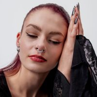 Frau mit geschlossenen Augen, trägt silbernen Kristall Septum Clicker, schwarze Kleidung