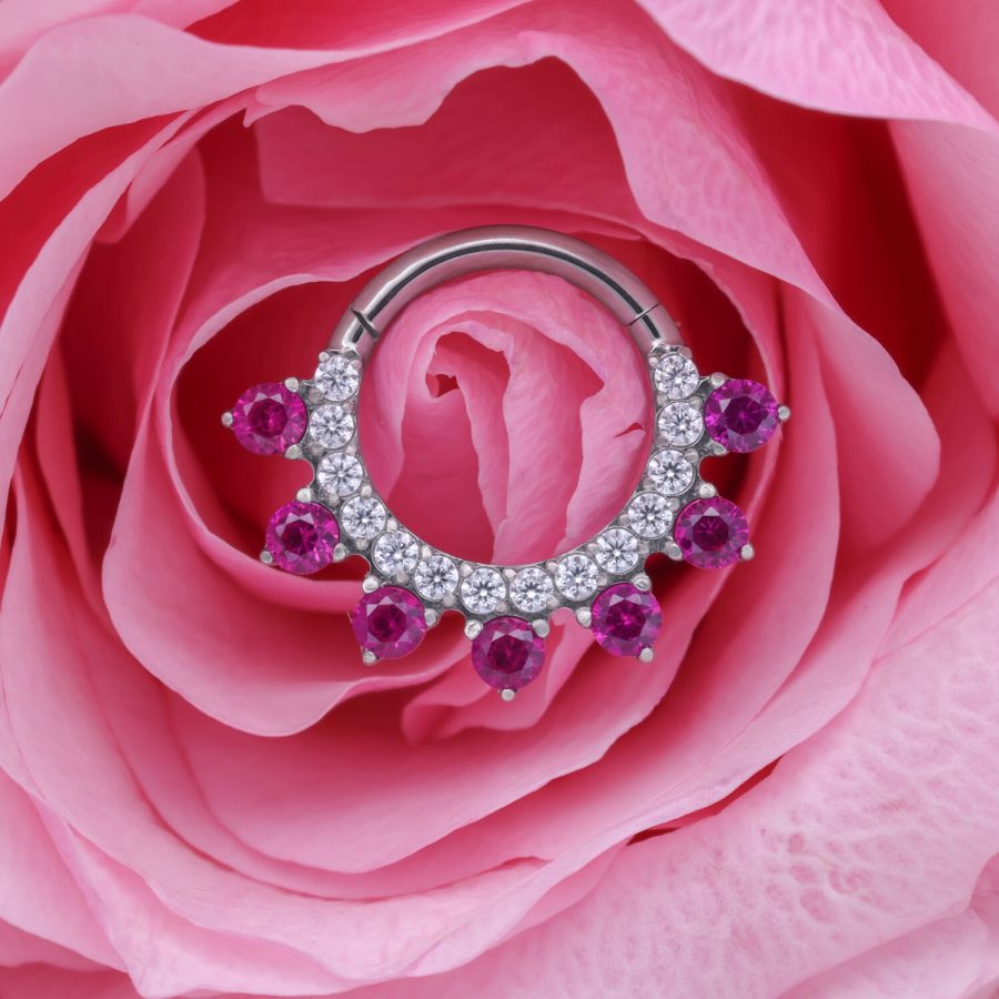 Silberner Piercingring mit roten Kristallen auf rosa Rosenblüte