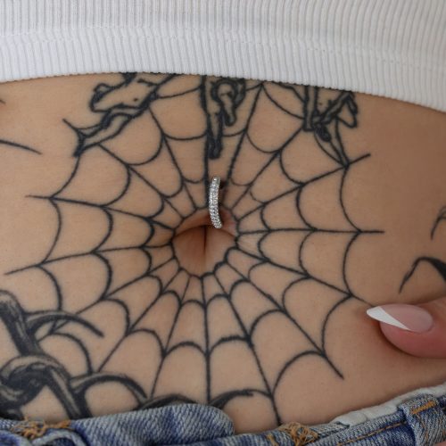 Bauchnabelpiercing mit silbernen Schmucksteinen in einer tätowierten Körpermitte
