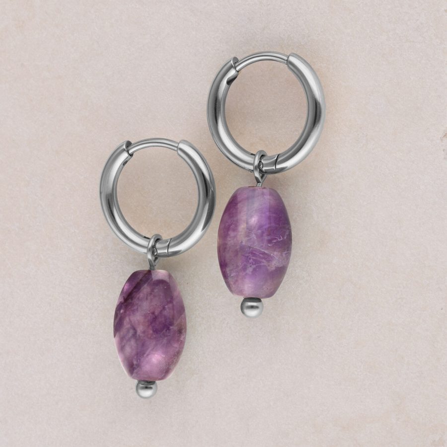 Zwei silberne Creolen mit violettem Amethystanhänger auf beigem Hintergrund