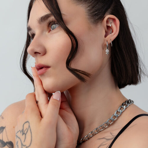 Frau mit Mini Lollipop Creolen, kurze Haare, Tattoos, weißer Hintergrund